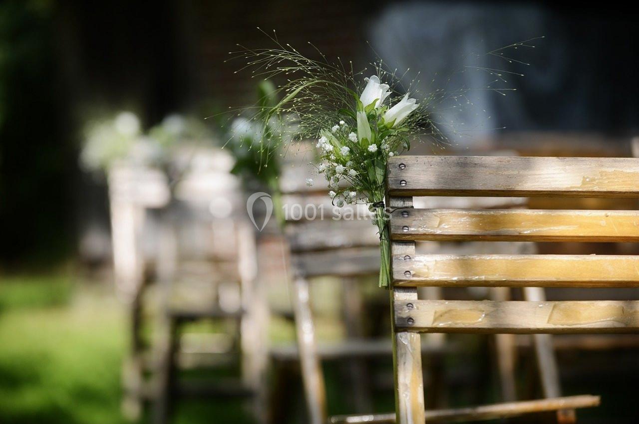 Chaises en bois alignées à l'extérieur, décorées de petites fleurs blanches et de verdure.