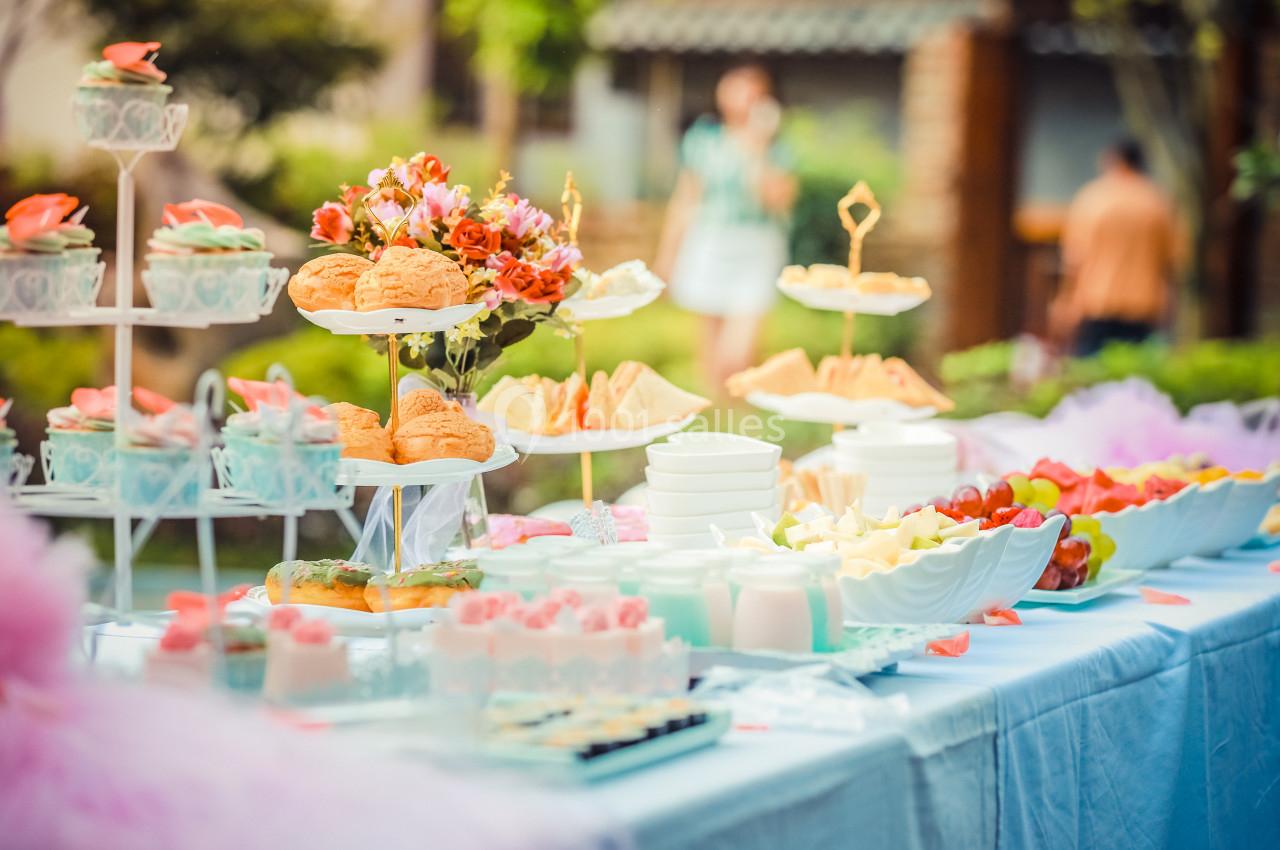 Table dressée en extérieur avec des pâtisseries, fruits, sandwiches et décorations florales.