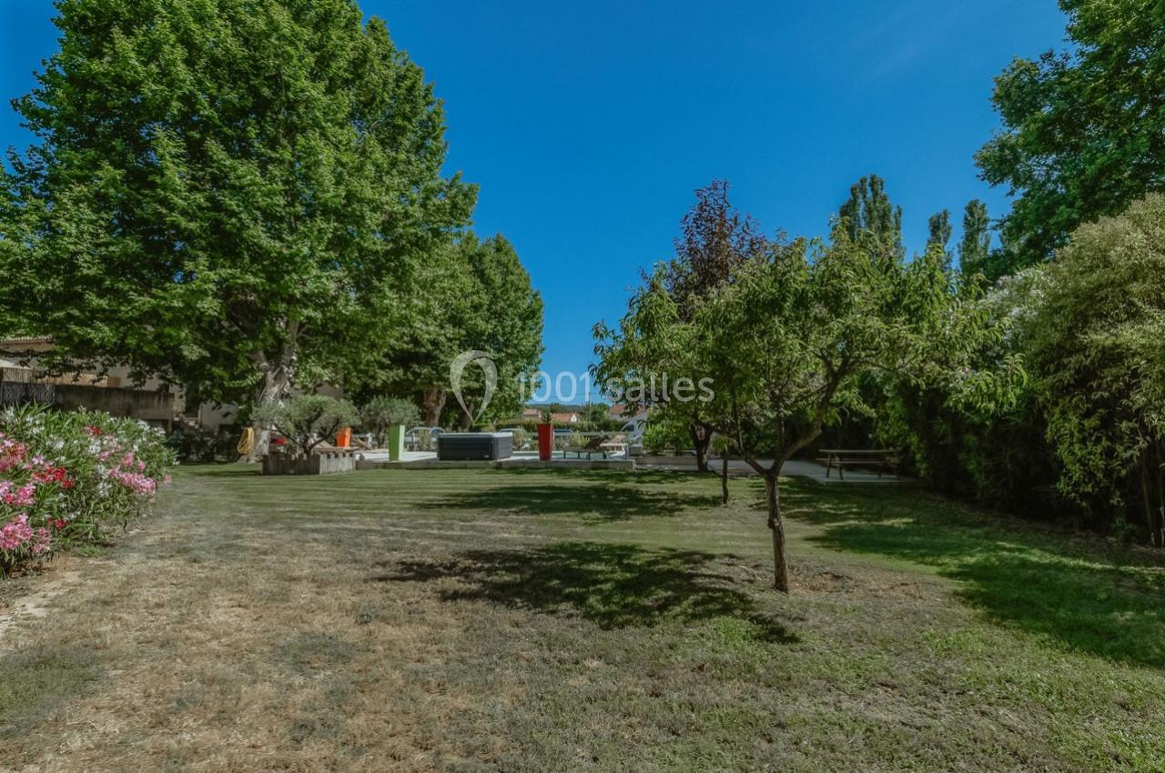 Jardin arboré avec pelouse, arbres variés et mobilier extérieur sous un ciel bleu clair.