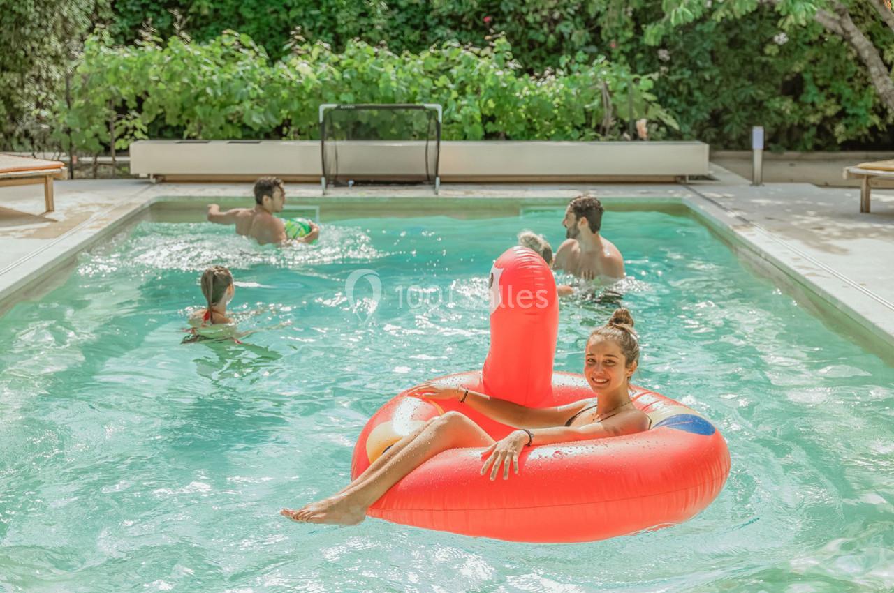 Une femme sur une bouée rouge dans une piscine, entourée de personnes nageant et jouant dans l'eau.