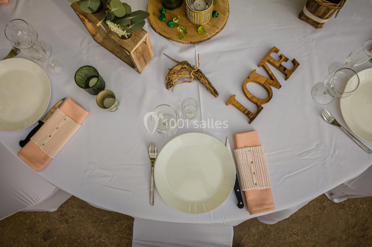 Table dressée avec nappes blanches, assiettes, couverts, serviettes roses et décorations en bois sur le thème de l'amour.