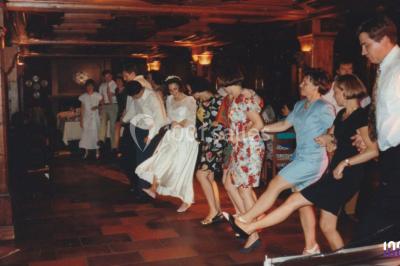 Salle sombre avec des poutres en bois, éclairée par des lumières colorées, des personnes discutent et se déplacent.