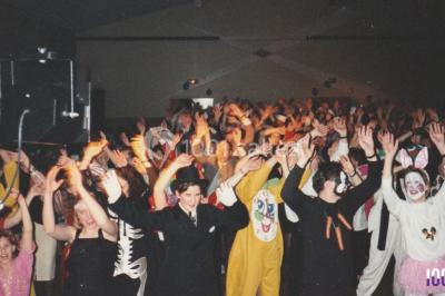 Salle sombre avec des poutres en bois, éclairée par des lumières colorées, des personnes discutent et se déplacent.
