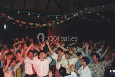 Salle sombre avec des poutres en bois, éclairée par des lumières colorées, des personnes discutent et se déplacent.