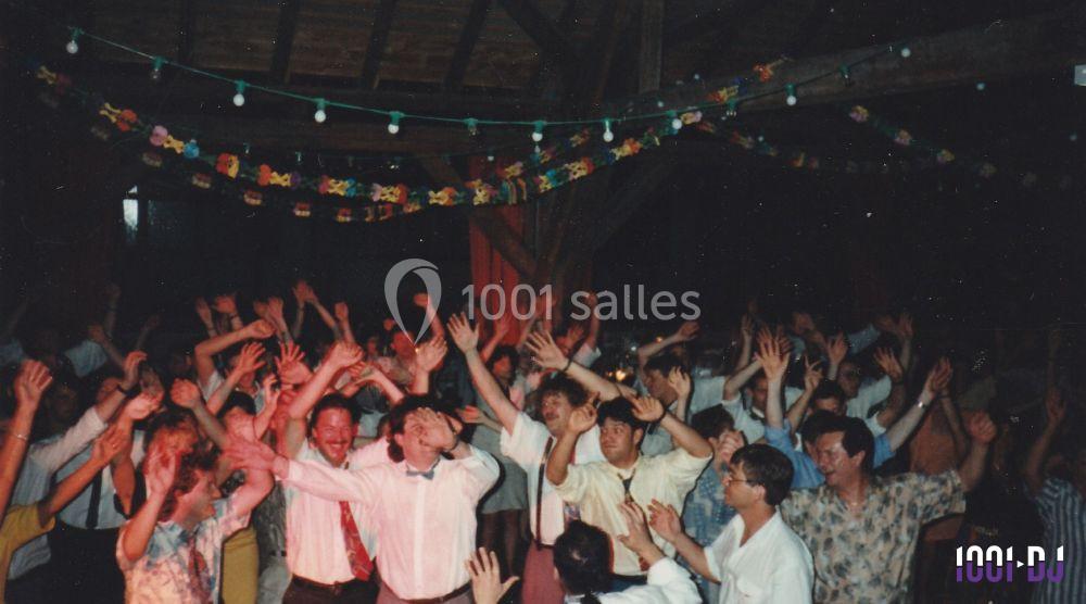 Groupe de personnes dansant et levant les bras sous des guirlandes lumineuses dans une salle en bois.