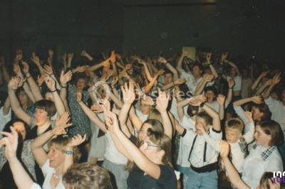 Salle sombre avec des poutres en bois, éclairée par des lumières colorées, des personnes discutent et se déplacent.