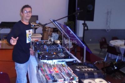 Salle sombre avec des poutres en bois, éclairée par des lumières colorées, des personnes discutent et se déplacent.