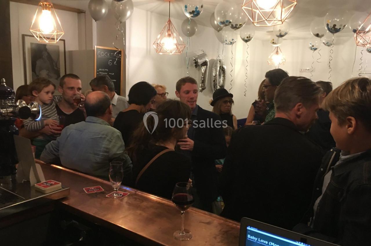 Groupe de personnes discutant dans un bar décoré avec des ballons et des guirlandes lors d'un événement festif.
