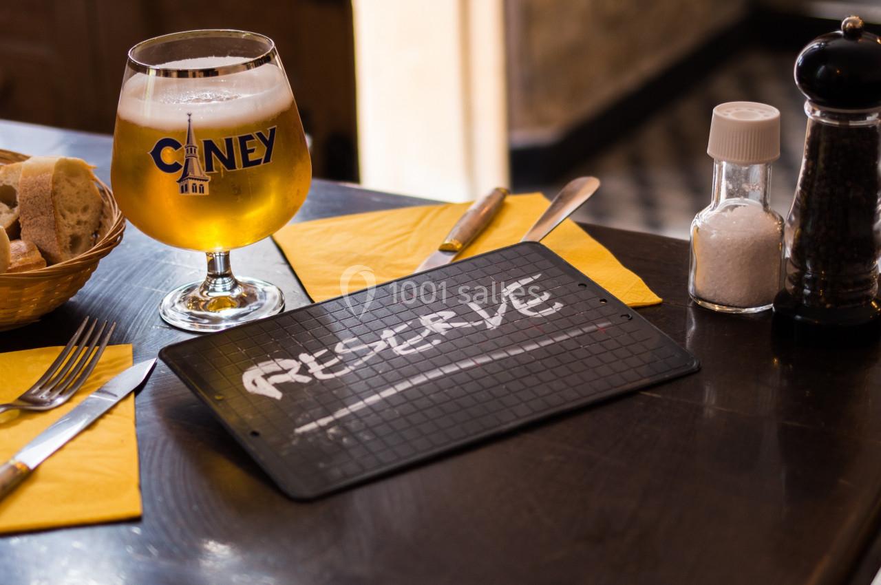 Verre de bière, panier de pain et plaque ’Réservé’ sur une table dressée avec couverts et serviettes jaunes.
