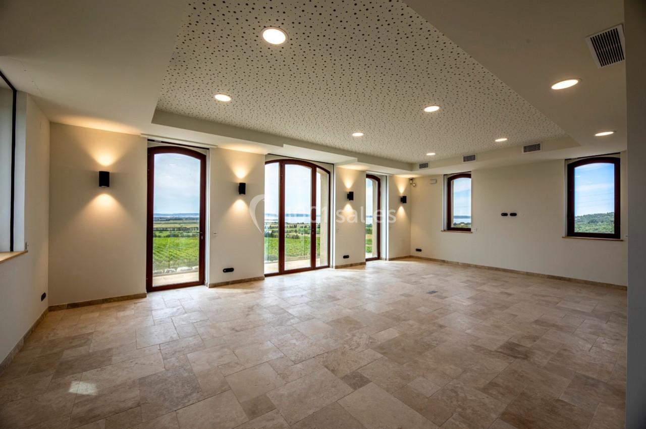 Salle lumineuse avec sol en pierre, grandes fenêtres cintrées donnant sur un paysage verdoyant et plafond perforé.