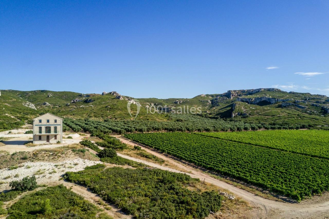 Vue aérienne d'une maison isolée entourée de vignes et de collines sous un ciel bleu dégagé.