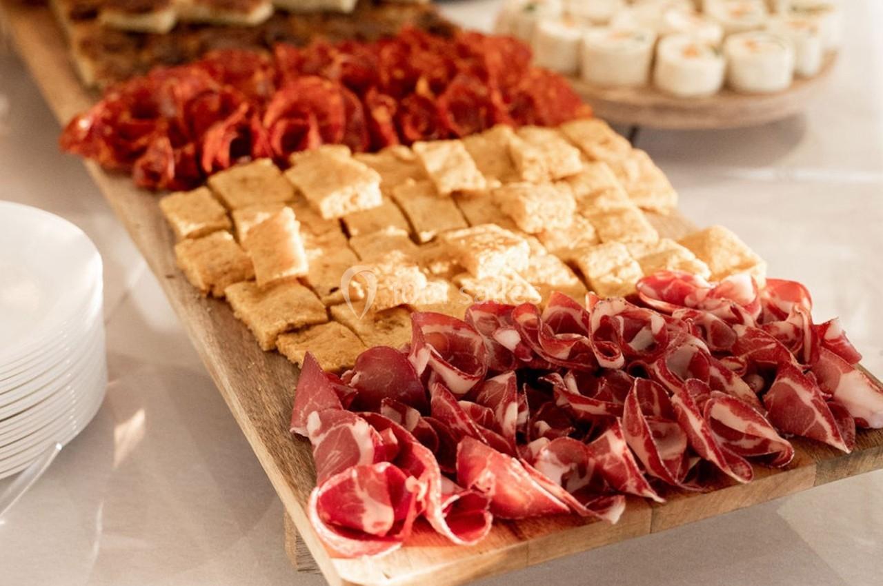 Plateau en bois garni de charcuteries variées et de petits morceaux de fromage, disposés pour un buffet.