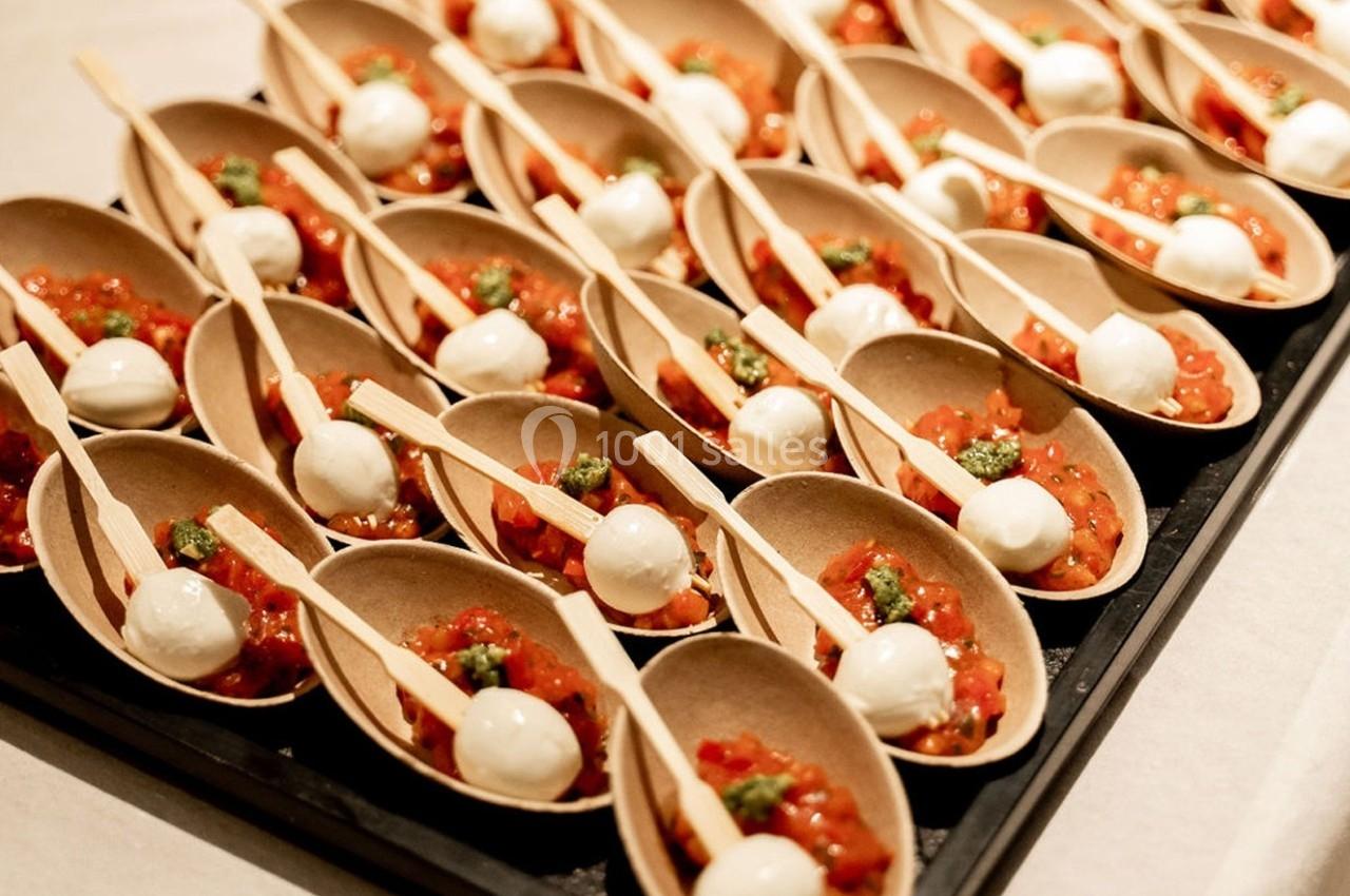 Cuillères en bois garnies de tomates, billes de mozzarella et pesto, disposées sur un plateau noir.