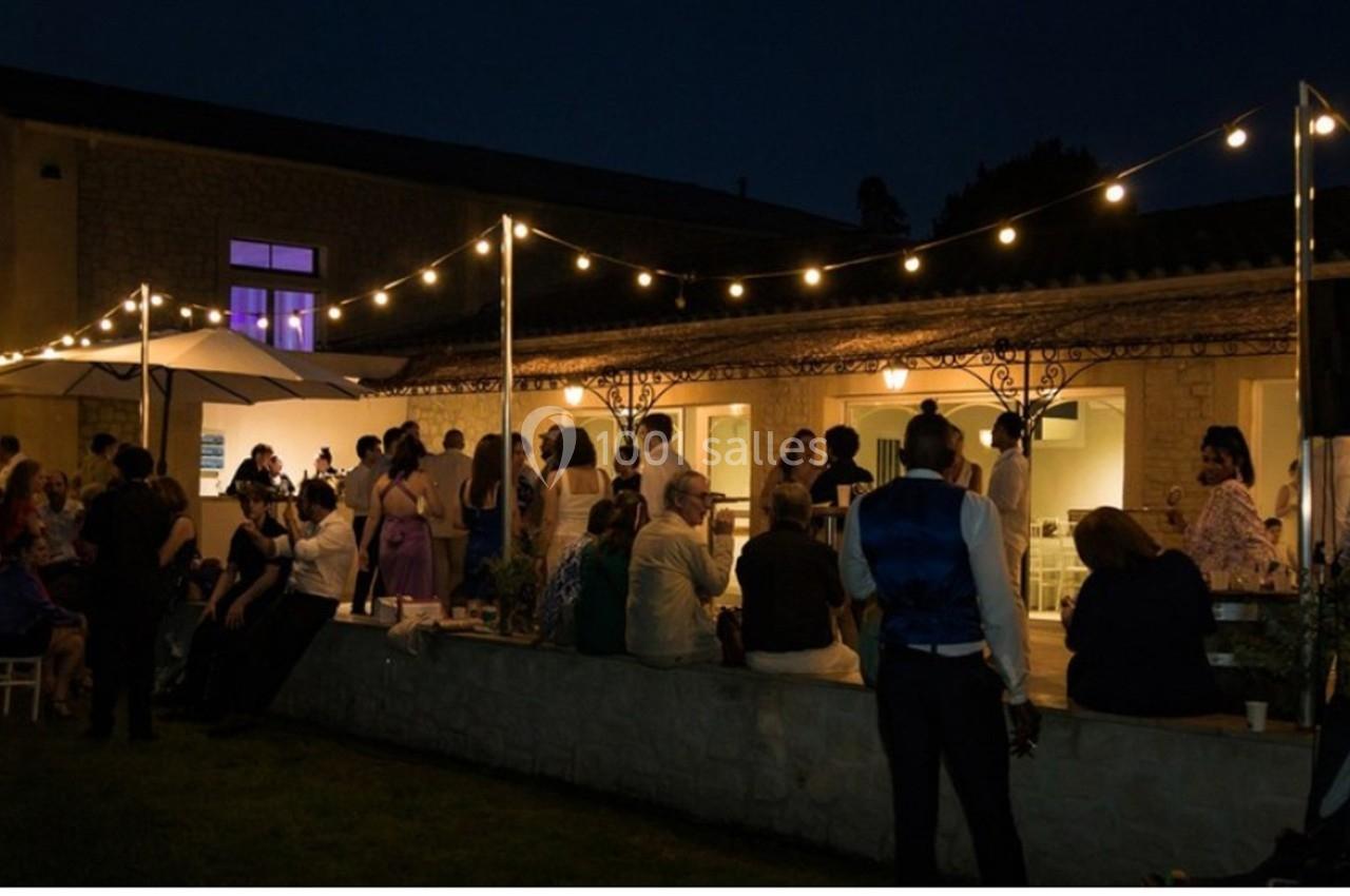 Groupe de personnes réunies en soirée dans une cour éclairée par des guirlandes lumineuses.