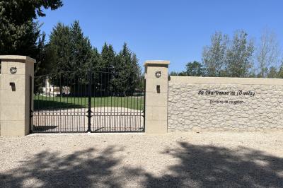 Portail en fer forgé noir et mur en pierre avec inscription ’Les Charbenes du Donelay, Domaine de réception’.