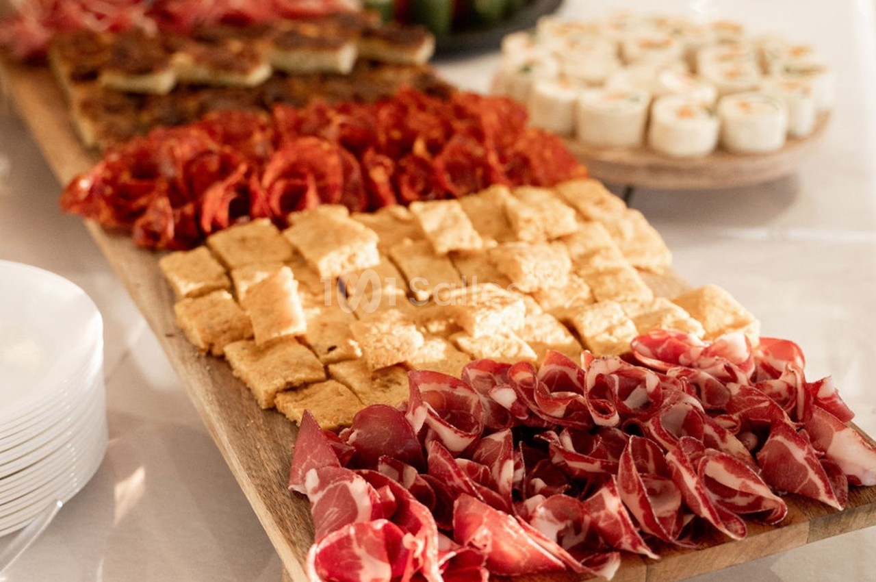 Plateau en bois garni de charcuterie, fromage, tapas et roulés apéritifs, disposés pour un buffet.
