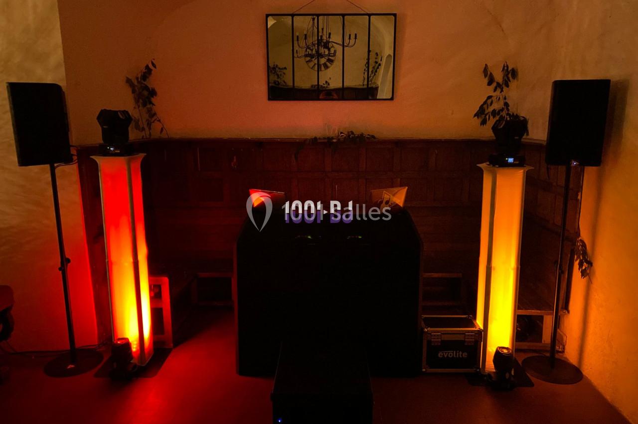 Console de DJ entourée de colonnes lumineuses rouges et jaunes dans une pièce sombre avec un miroir au mur.