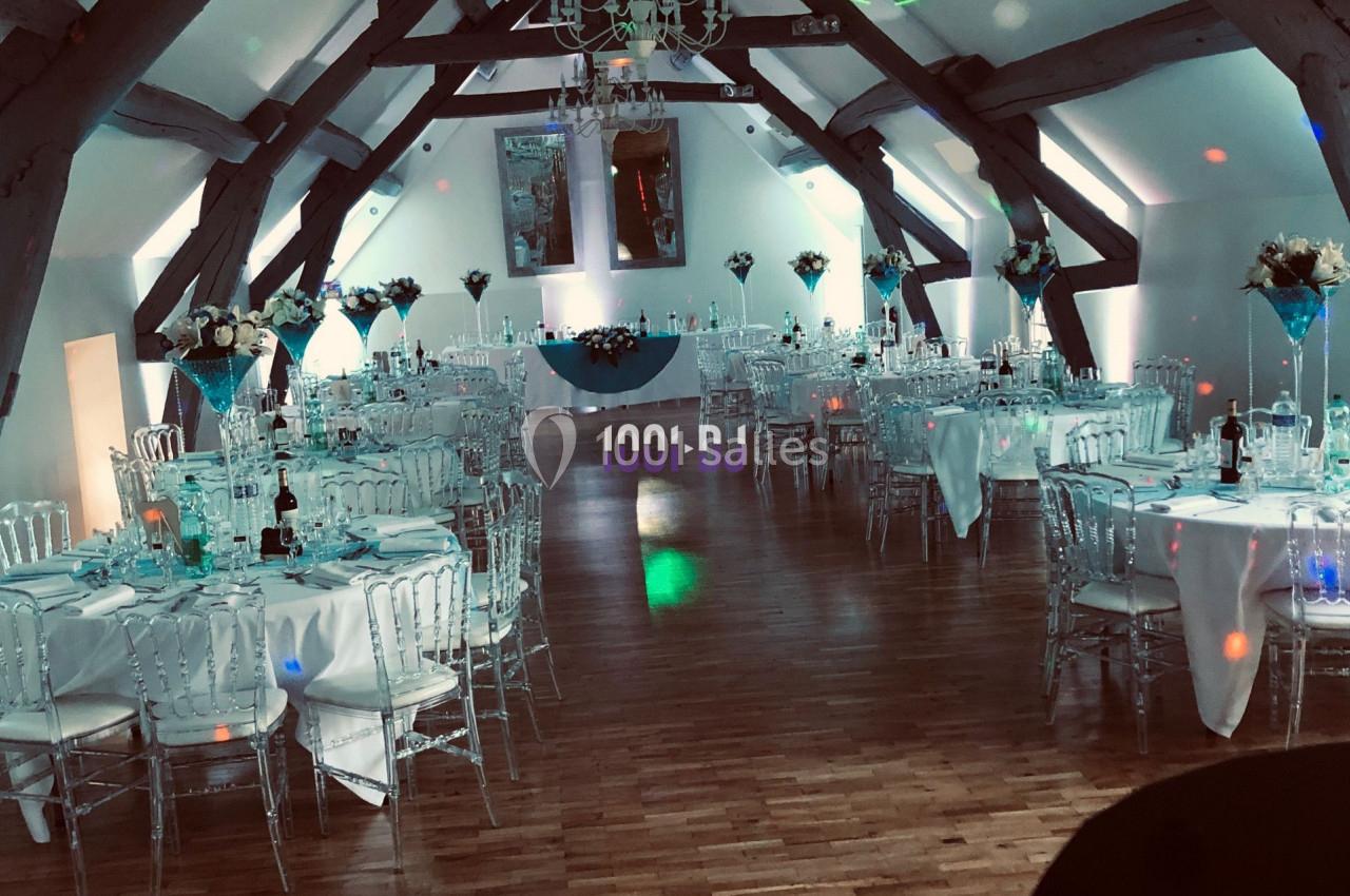 Salle de réception décorée avec des tables dressées, des chaises transparentes et des lumières colorées sur le parquet.