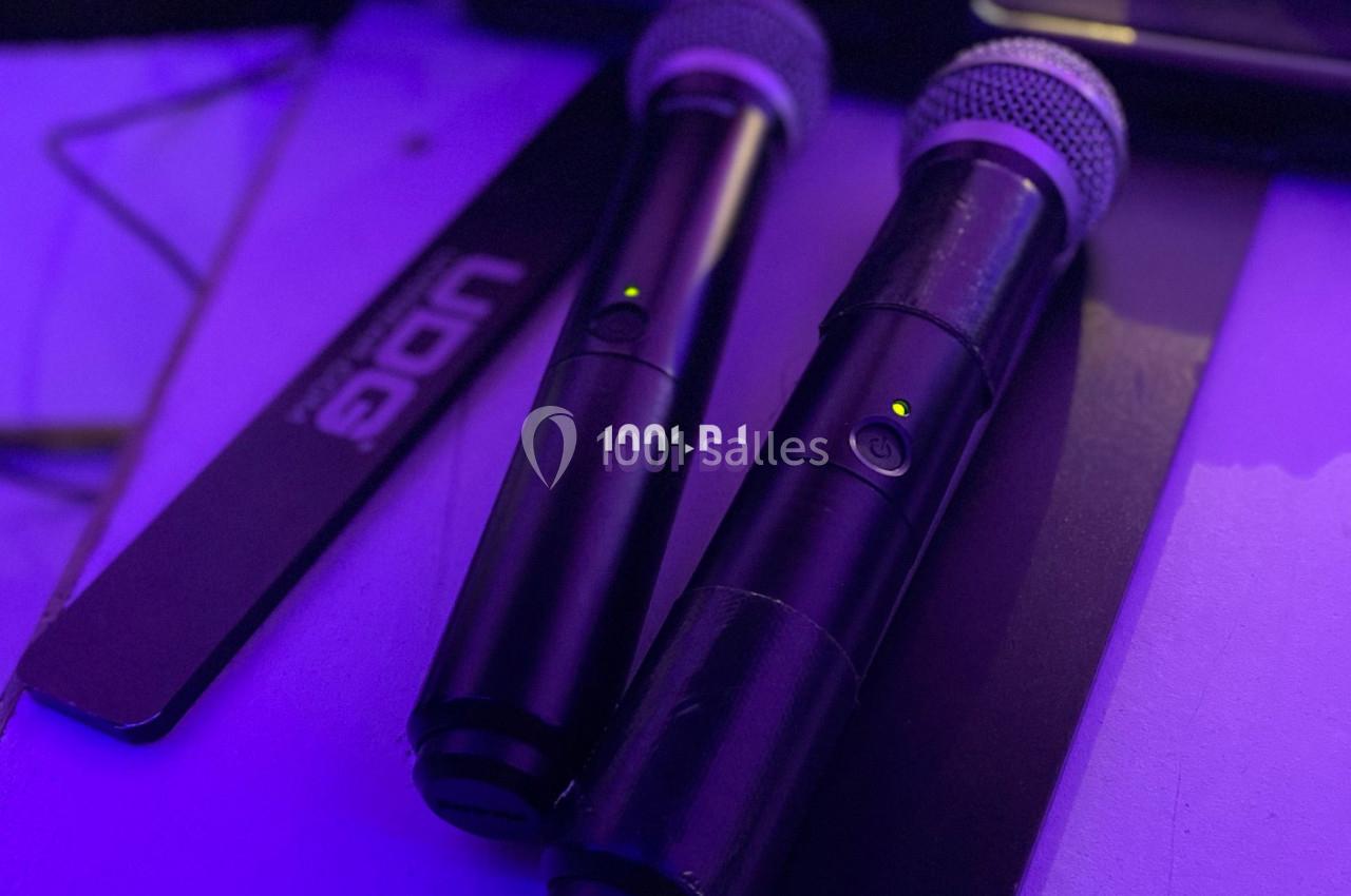 Deux microphones sans fil noirs posés sur une surface éclairée par une lumière violette.