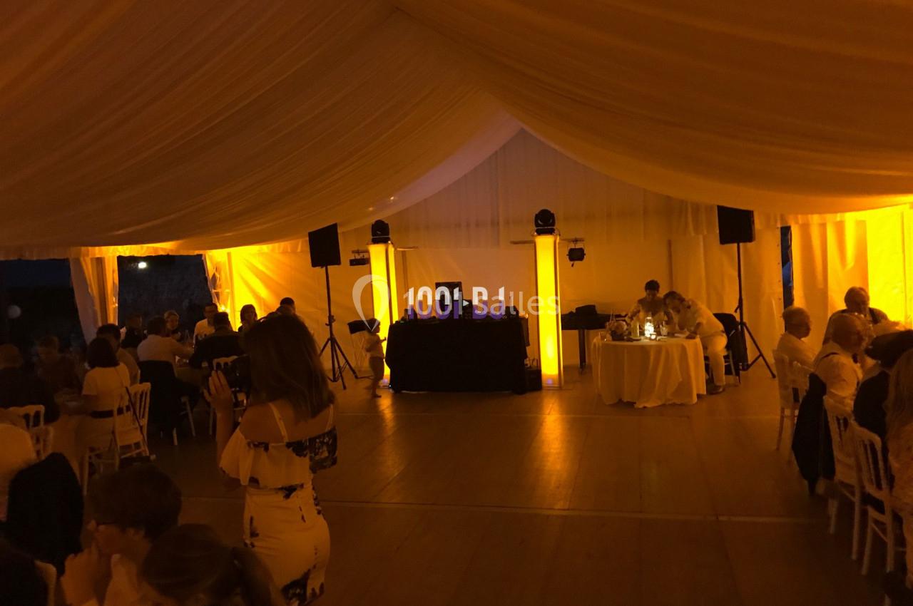 Salle de réception éclairée en jaune avec des invités assis, une piste de danse et une table de DJ au fond.