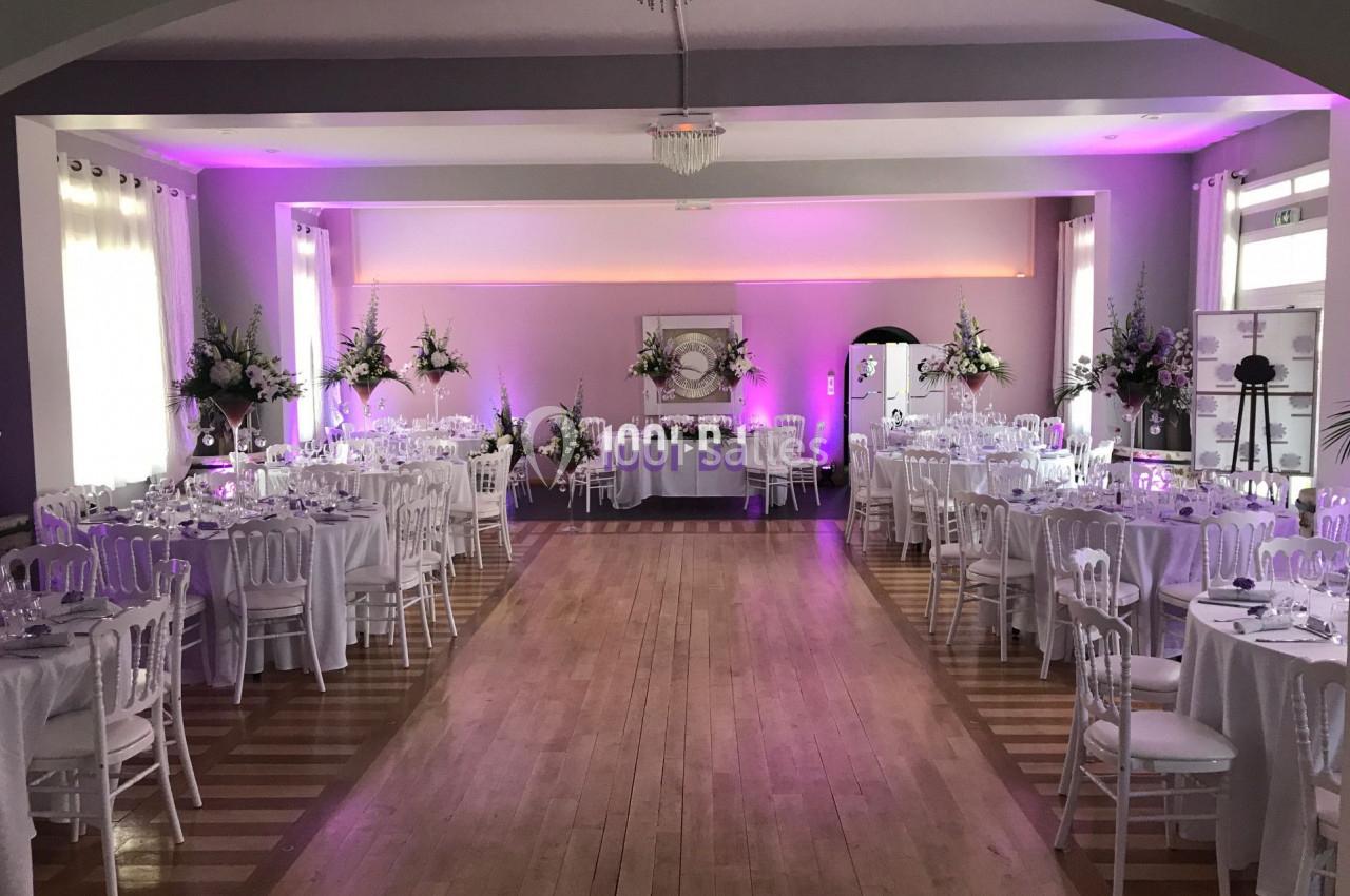 Salle de réception décorée avec des tables rondes, des chaises blanches et un éclairage rose.