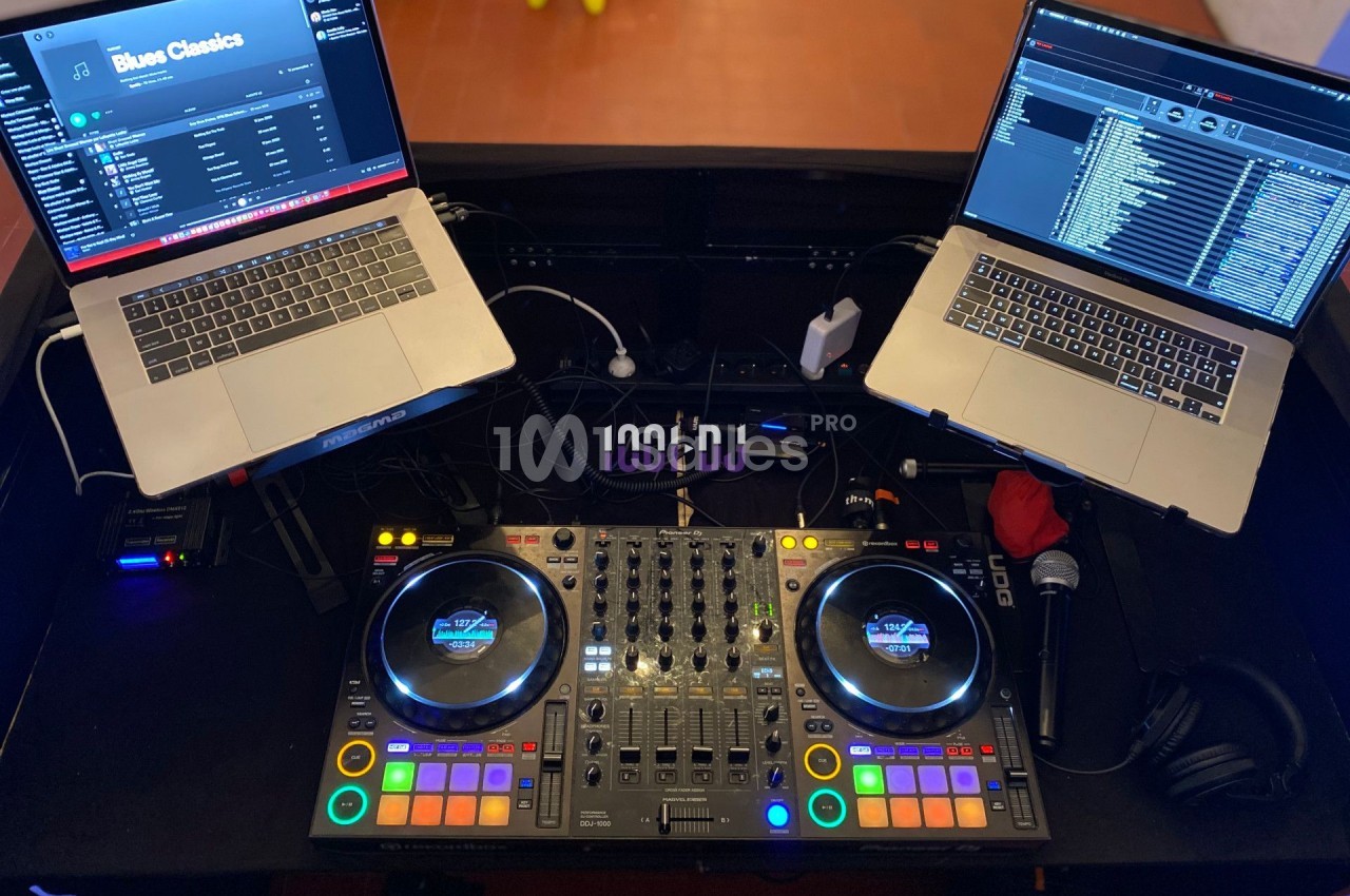 Deux ordinateurs portables et une console de mixage DJ avec des câbles et accessoires sur une table.