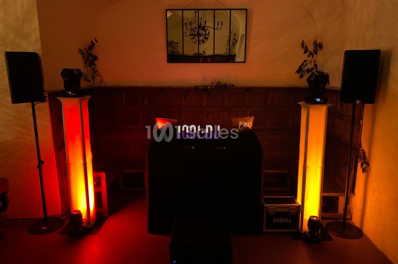 Console de DJ entourée de colonnes lumineuses rouges et jaunes dans une pièce sombre avec un miroir au mur.