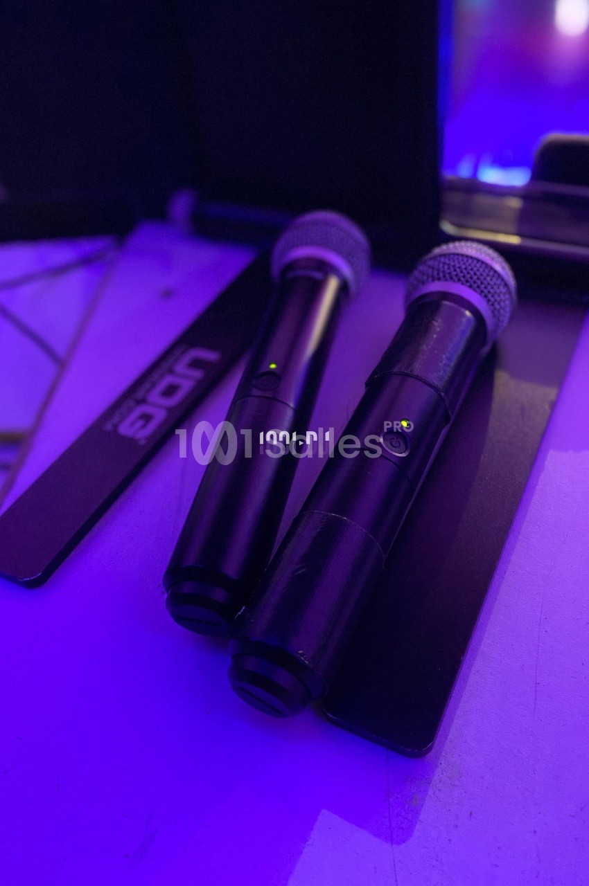 Deux microphones sans fil noirs posés sur une surface éclairée par une lumière violette.
