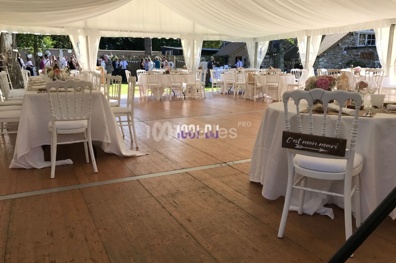 Intérieur d'une tente de réception avec tables et chaises blanches, décorée pour un événement en plein air.