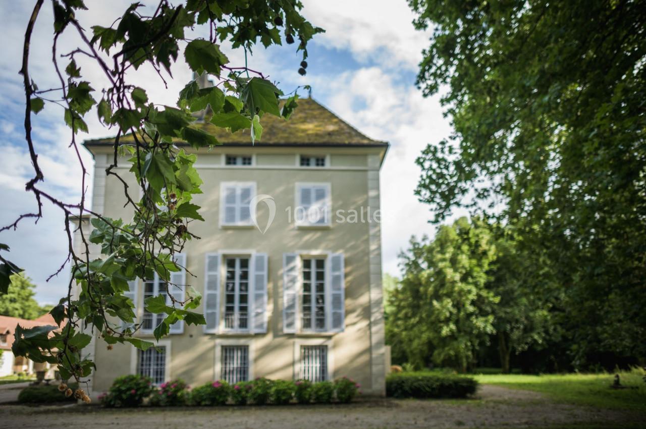 Façade d'une maison ancienne à trois étages, entourée de verdure, sous un ciel partiellement nuageux.