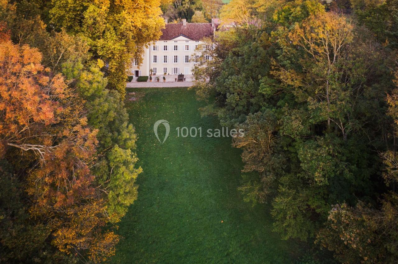 Vue aérienne d'un manoir entouré d'arbres aux couleurs automnales, avec une pelouse verdoyante au premier plan.