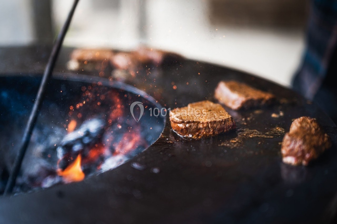 Viande en train de griller sur une plaque chauffante ronde au-dessus d'un feu ouvert.