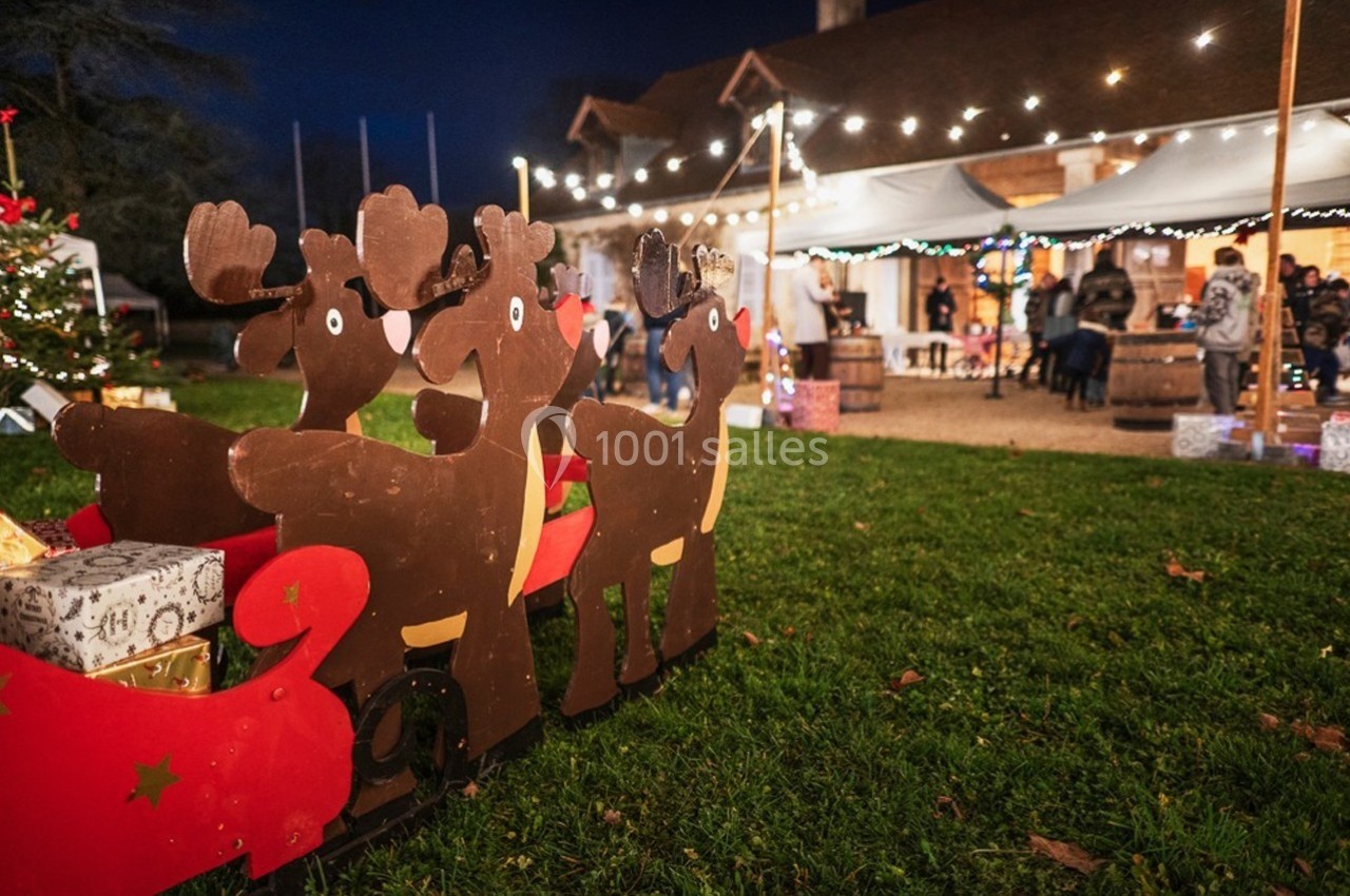 Décoration en bois représentant des rennes et un traîneau, avec des cadeaux, devant un marché de Noël illuminé.
