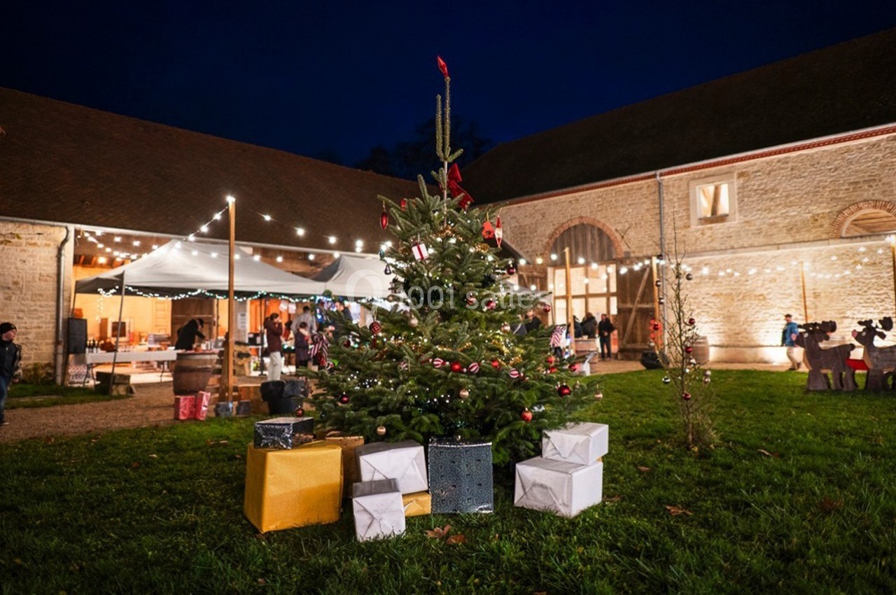 Sapin de Noël décoré avec des cadeaux à sa base, installé dans une cour éclairée par des guirlandes lumineuses.