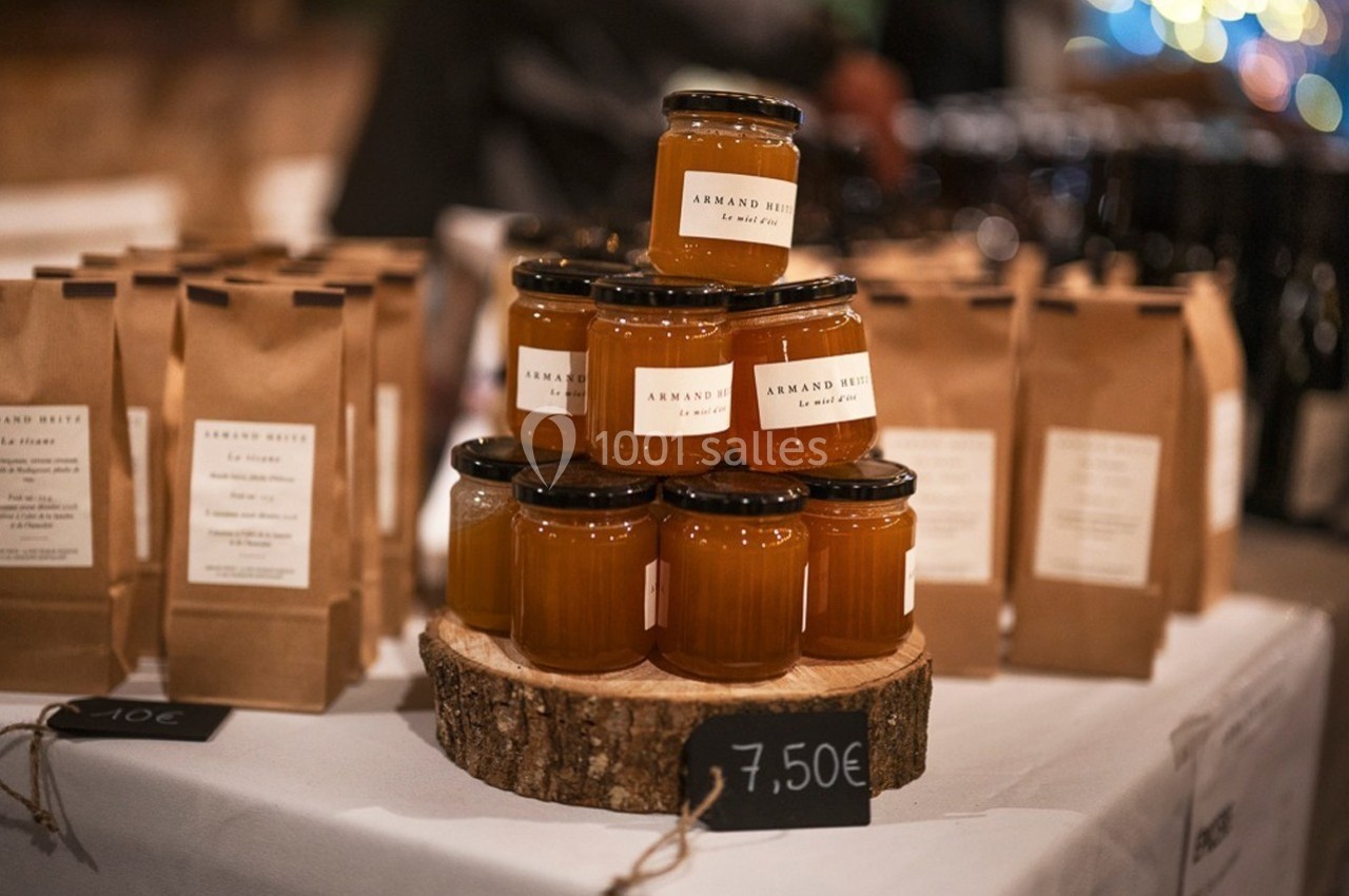Pots de confiture disposés en pyramide sur une tranche de bois, entourés de sachets en papier sur une table.