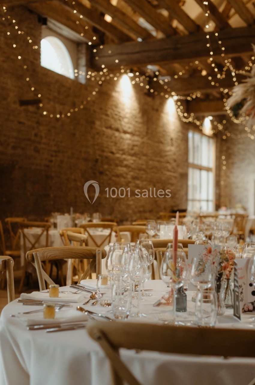 Salle de réception décorée avec des guirlandes lumineuses, des tables dressées et des chaises en bois.