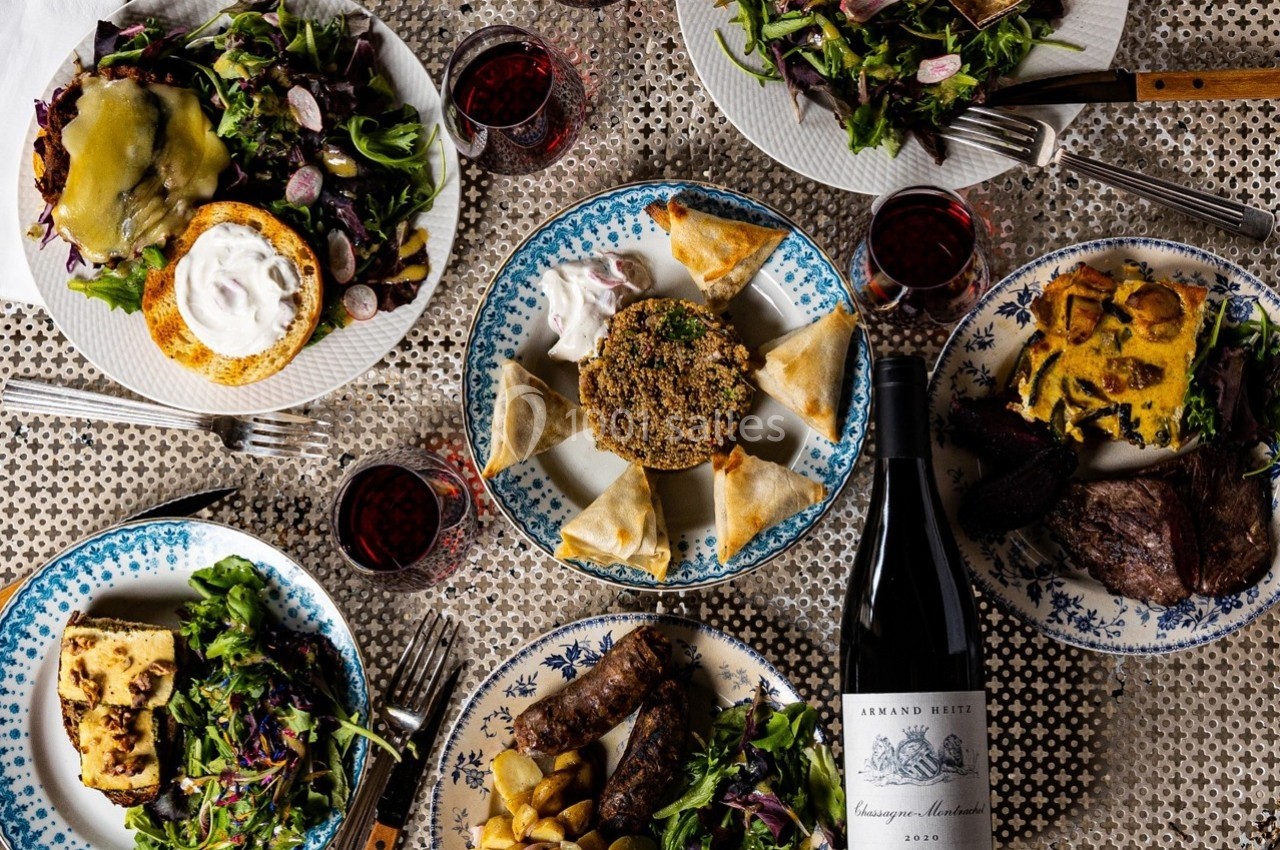 Table dressée avec des assiettes variées de plats, accompagnées de verres de vin rouge et d'une bouteille de vin.