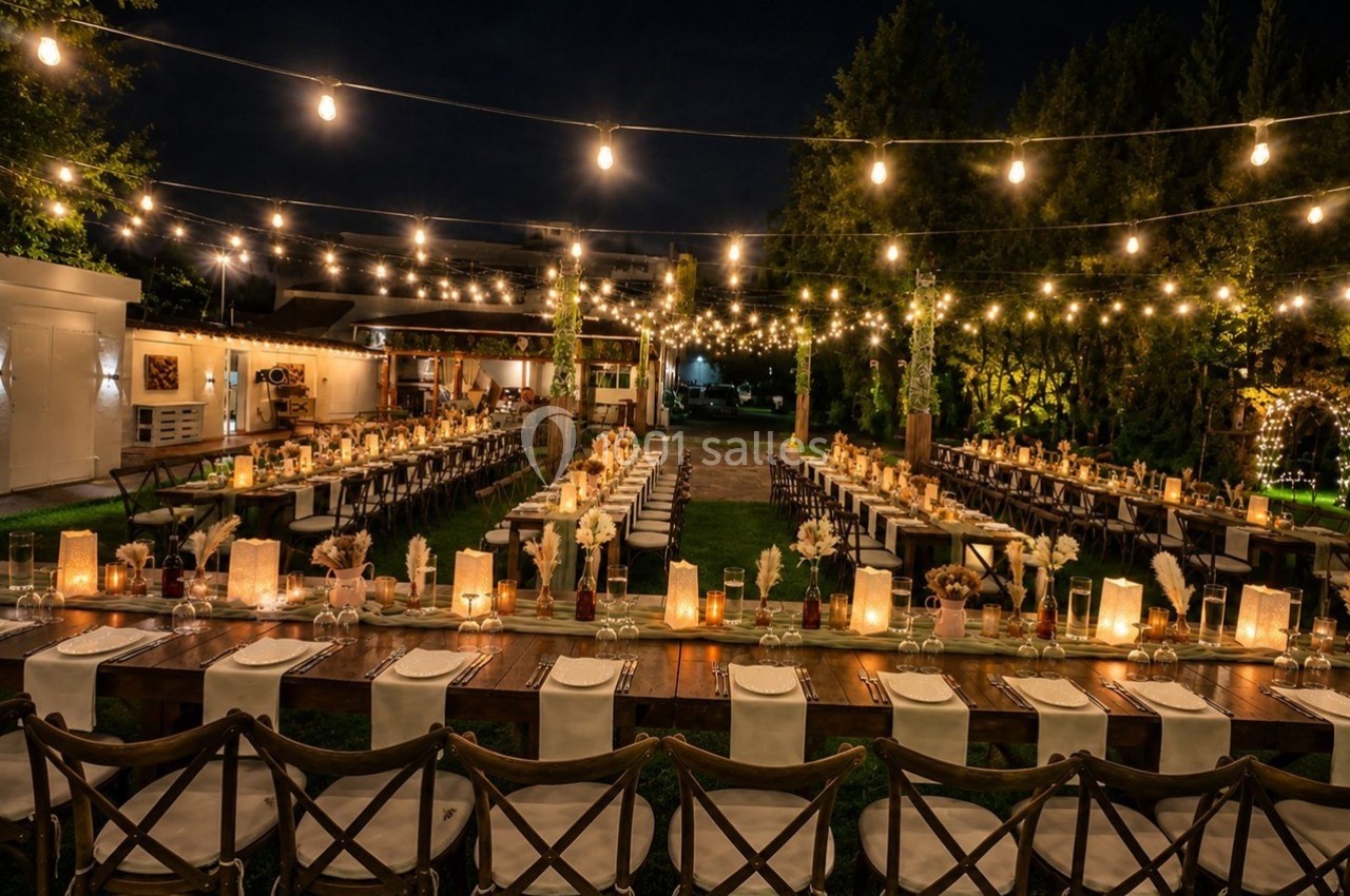 Tables de réception décorées avec des bougies et des fleurs sous des guirlandes lumineuses dans un jardin de nuit.