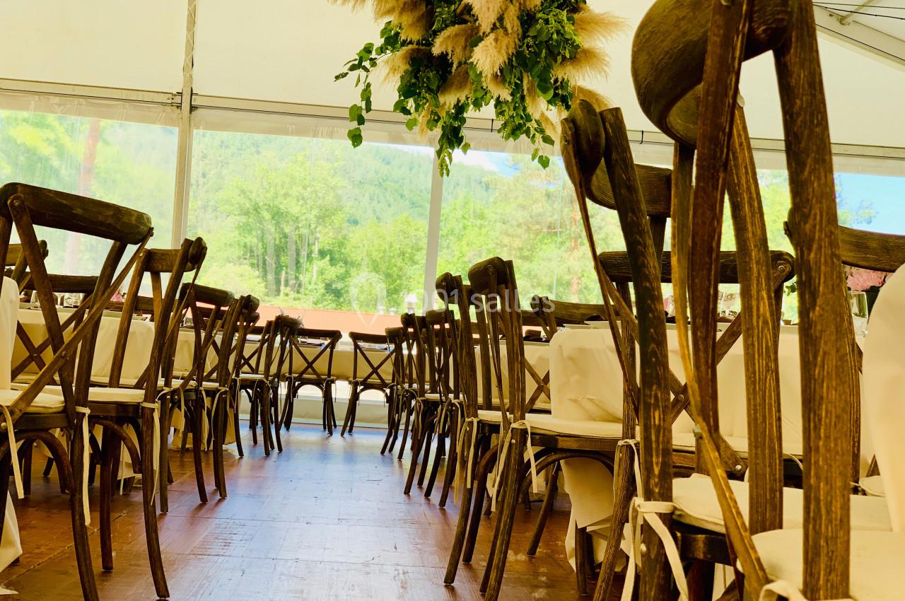 Salle de réception avec des chaises en bois disposées autour de tables, décorée de suspensions végétales.