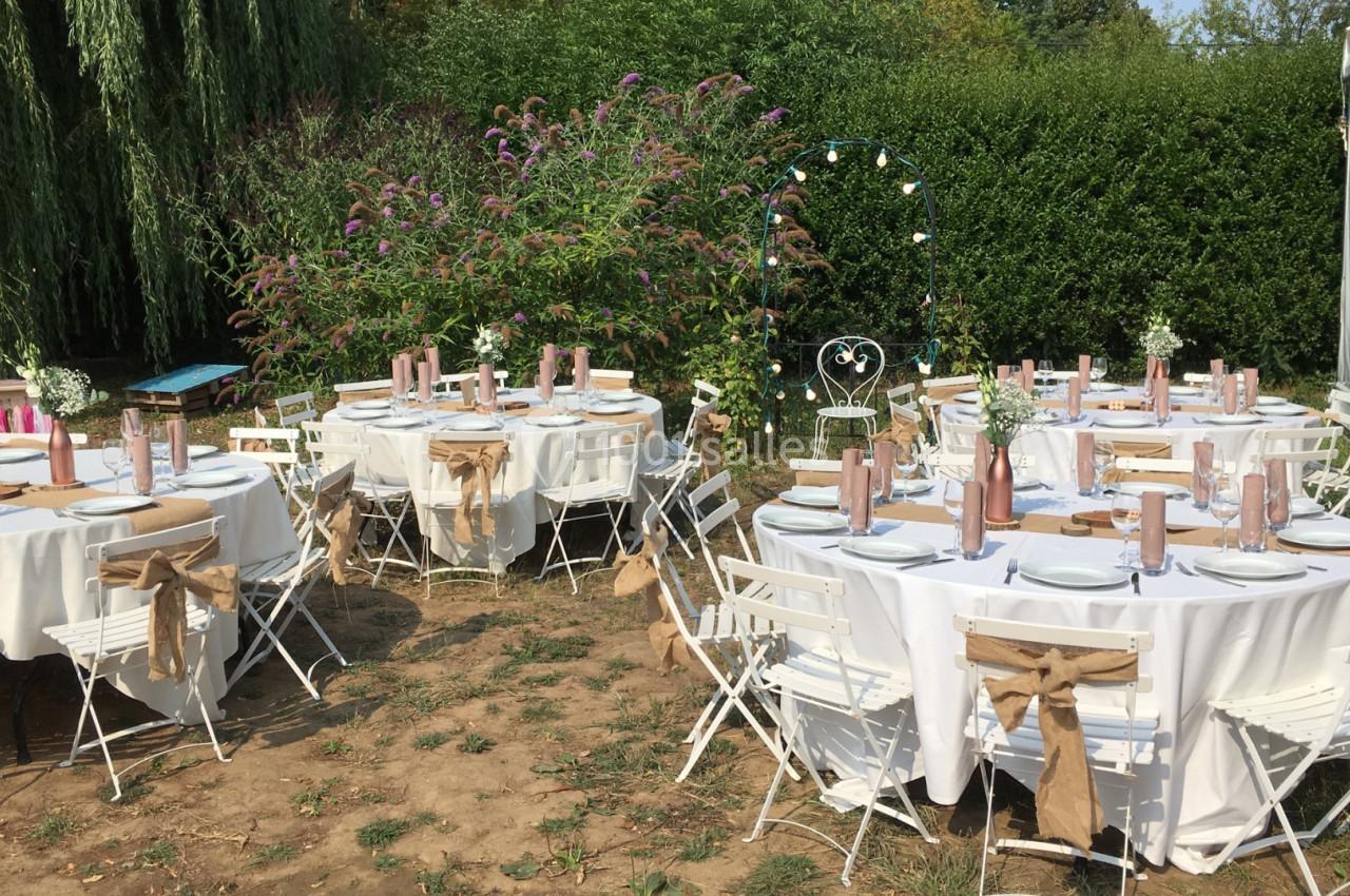 Tables rondes décorées pour un événement en plein air, entourées de chaises blanches et de verdure.