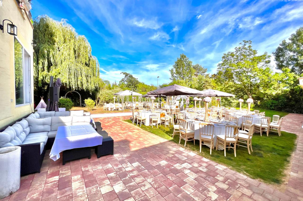 Terrasse aménagée avec des tables et chaises en bois, parasols, canapés et végétation environnante sous un ciel dégagé.