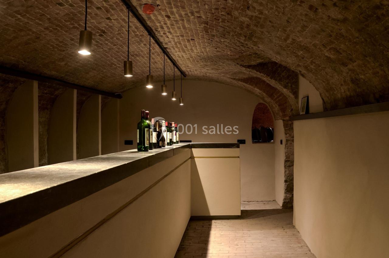 Cave voûtée en briques avec un comptoir éclairé et des bouteilles disposées dessus.