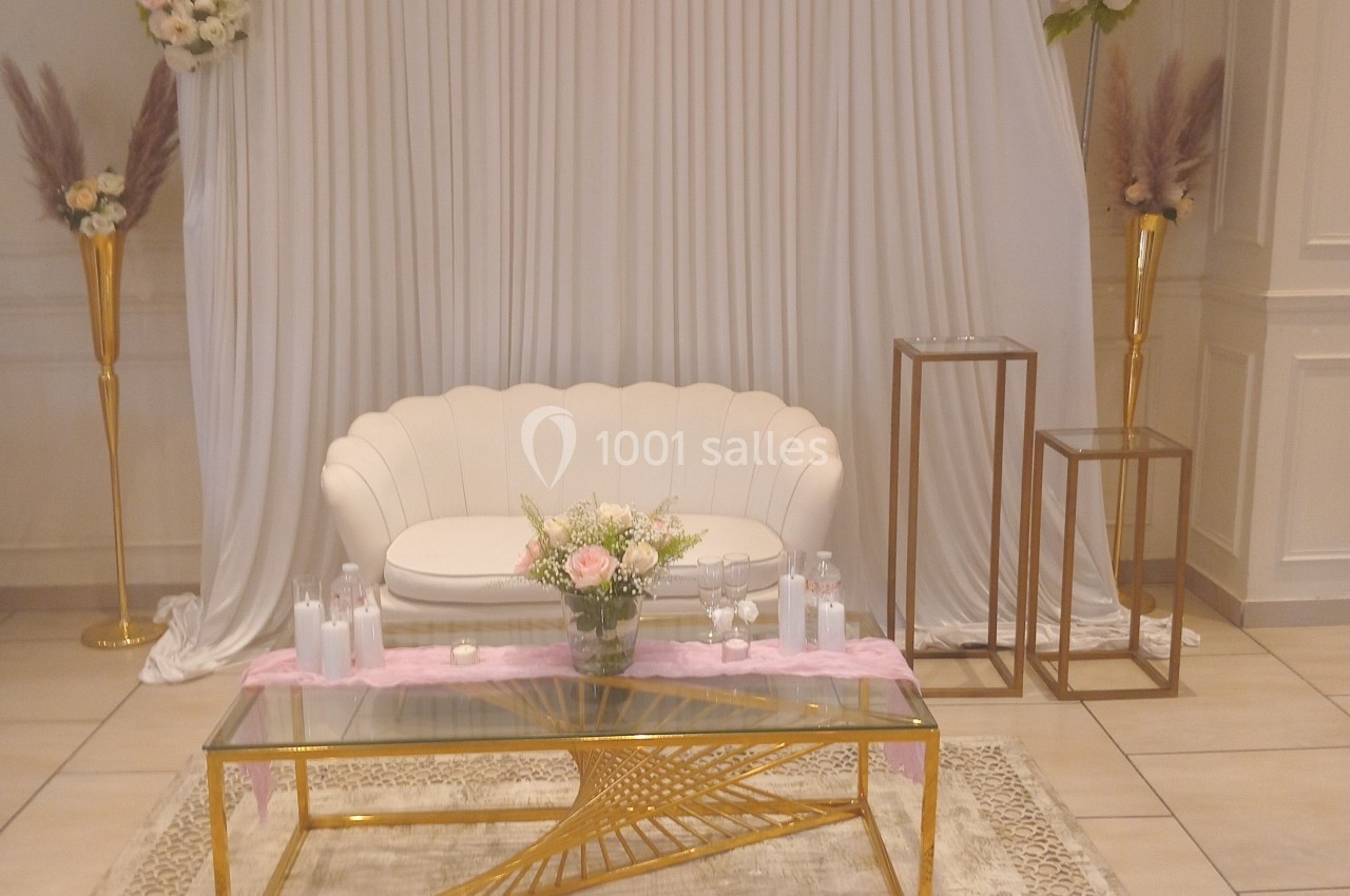 Décor élégant avec canapé blanc, table dorée, fleurs roses et blanches, et éléments décoratifs dans une salle lumineuse.