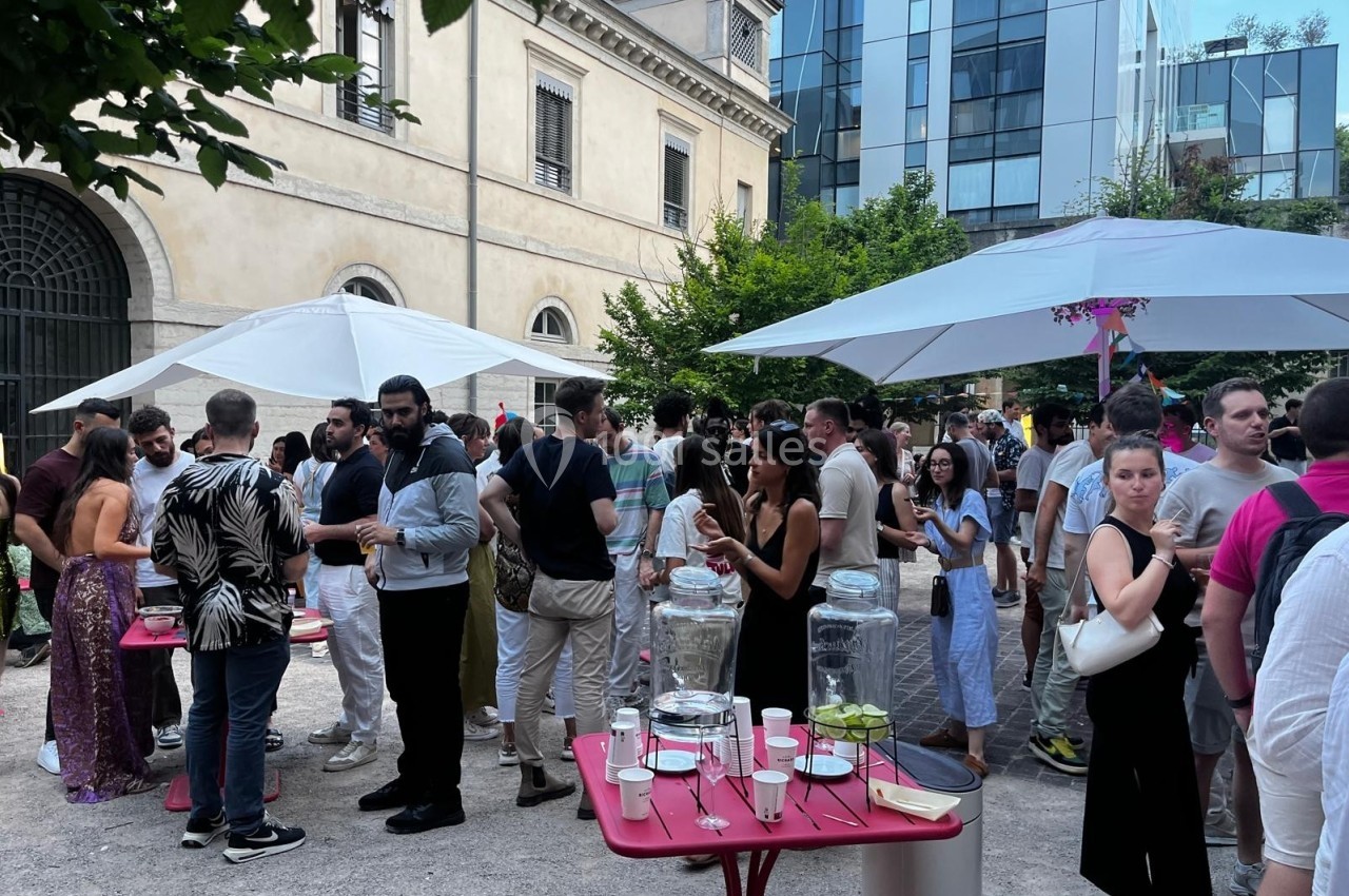 Groupe de personnes discutant et partageant un moment convivial dans une cour extérieure avec parasols et tables.