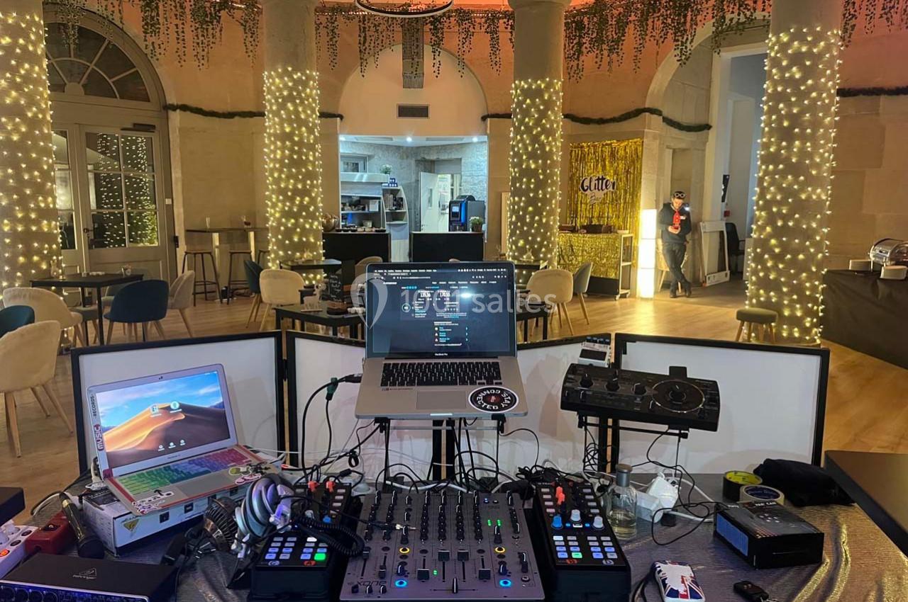 Poste de DJ avec table de mixage, ordinateurs et contrôleurs, installé dans une salle décorée de guirlandes lumineuses.