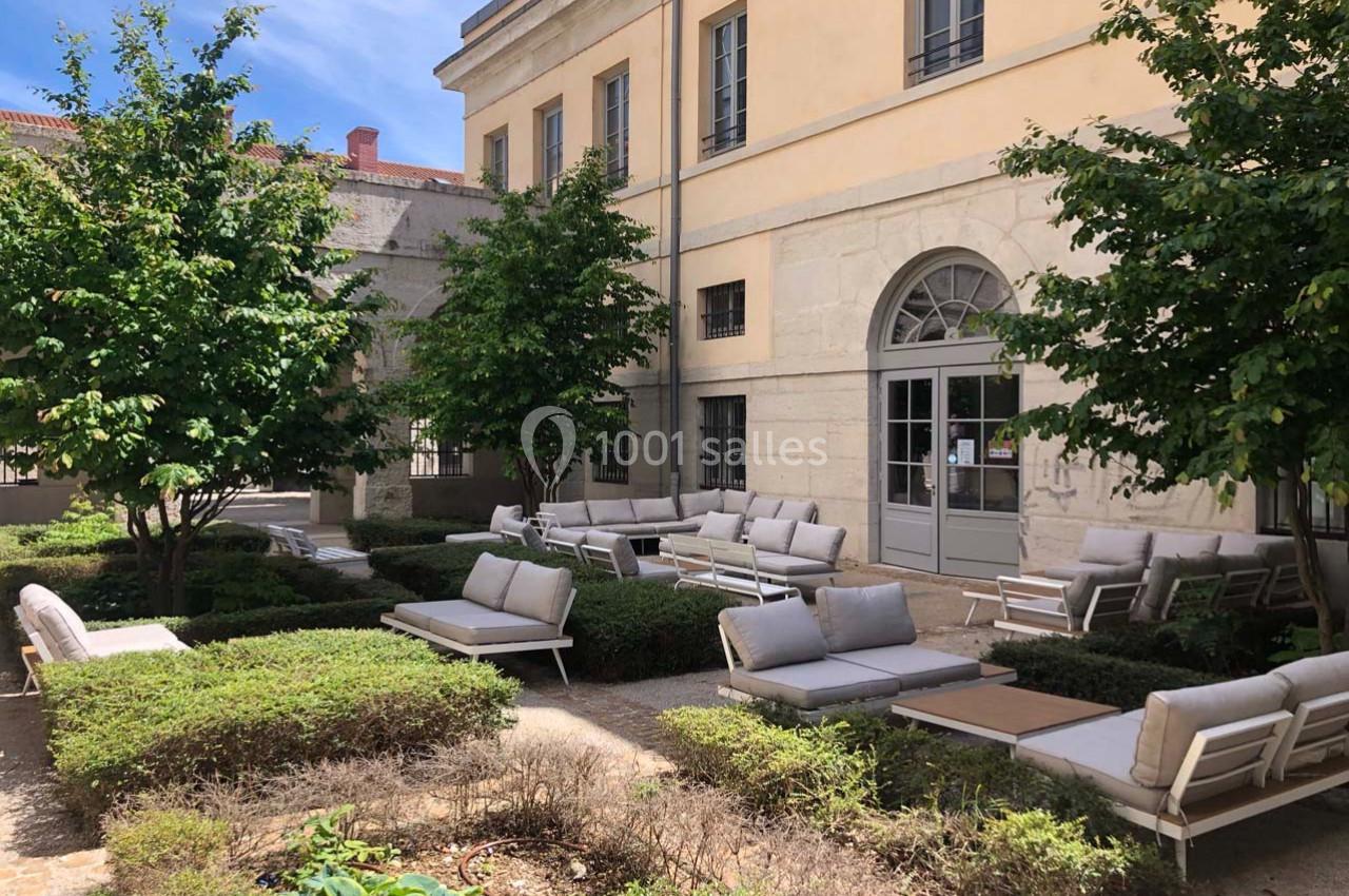 Cour intérieure avec mobilier de jardin moderne, entourée de buissons taillés et d'arbres, devant un bâtiment en pierre.