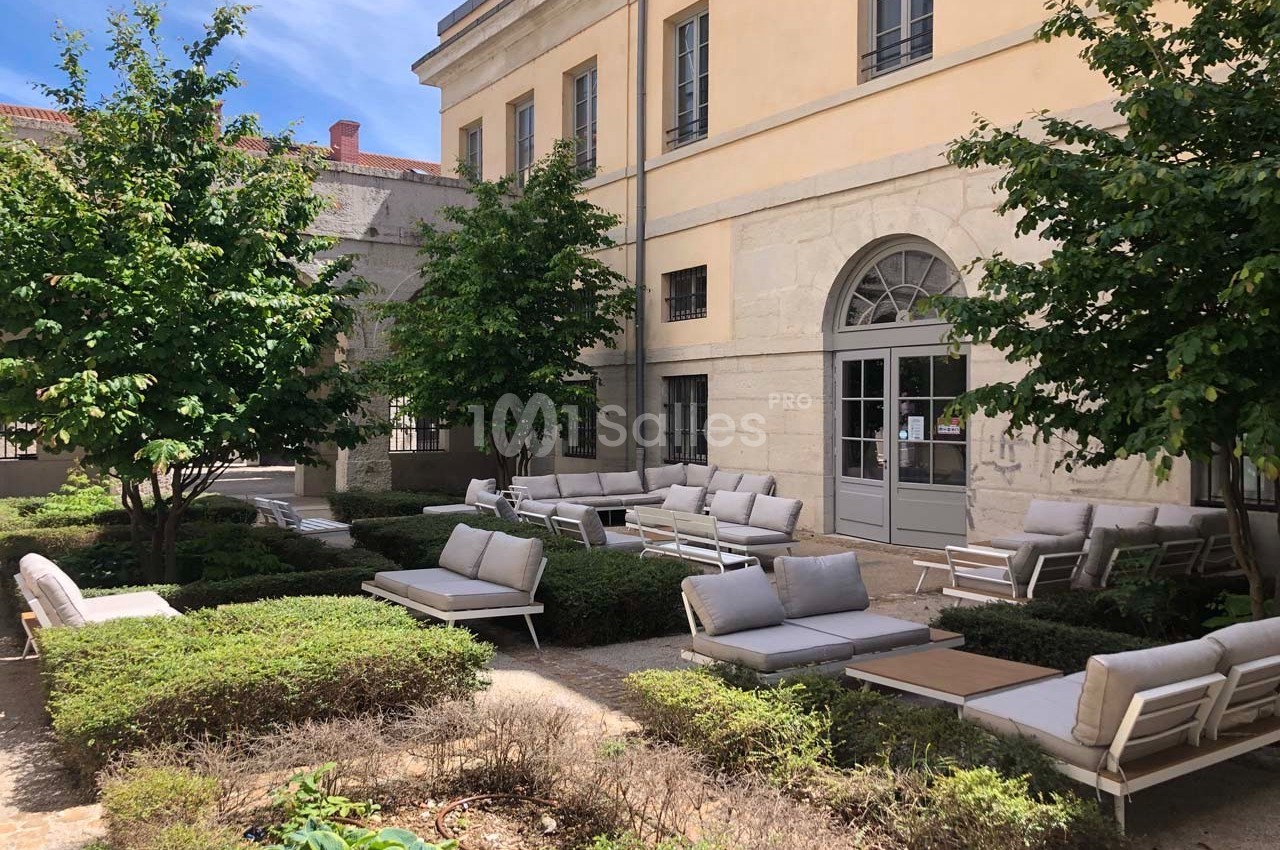 Cour intérieure avec mobilier de jardin moderne, entourée de buissons taillés et d'arbres, près d'un bâtiment en pierre.