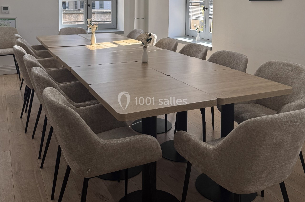 Salle de réunion lumineuse avec une grande table en bois entourée de chaises rembourrées et des vases décoratifs.