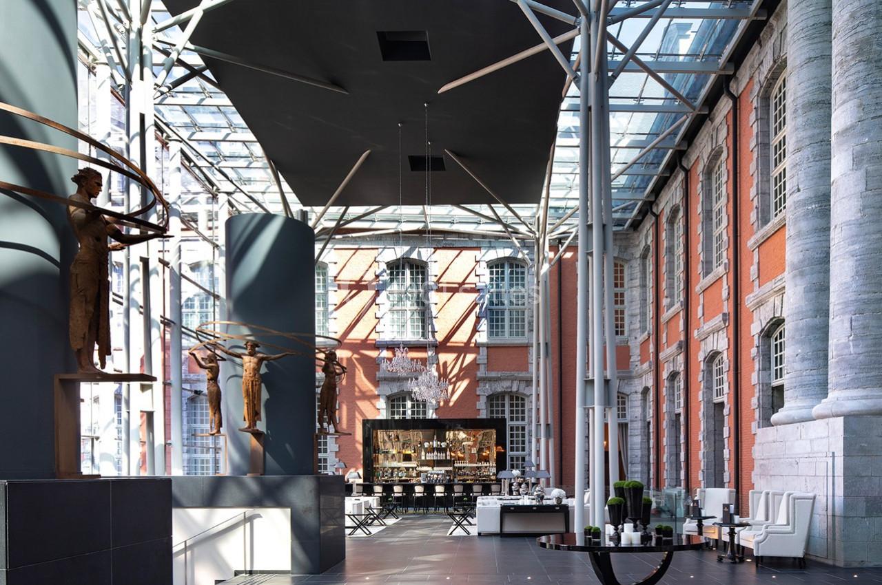 Intérieur d'un bâtiment avec verrière, sculptures modernes, murs en briques rouges et espace aménagé avec tables.