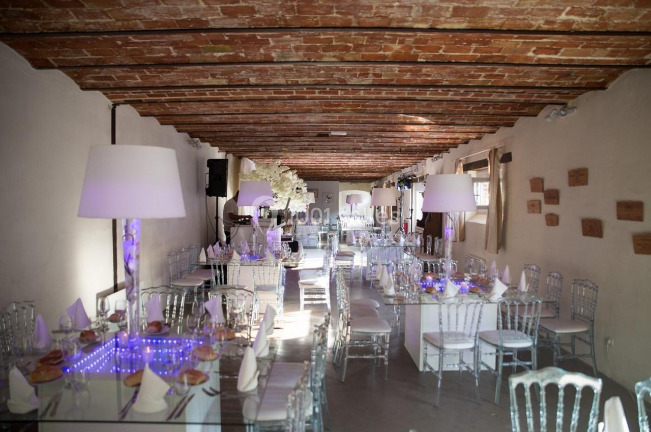 Salle de réception décorée avec des tables en verre, chaises transparentes et éclairage tamisé sous un plafond en briques.